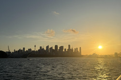 Blick über das Wasser von einem Boot. Das Skyline von Sydney im Sonnenuntergang.