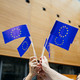 EU Flaggen Menschen stehen in einem Kreis und halten kleine EU-Flaggen in der Luft.