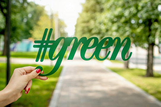 artem-beliaikin-BpQ-ClsKeXg-unsplash.jpg eine Person hält den Schriftzug "#green", mit einem Park im Hintergrund an einem sonnigen Tag