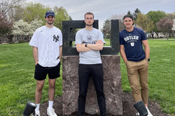 3 Männer stehen draußen vor dem "BU" Schild der Butler University und tragen Kleidungsstücke mit "Butler" drauf.